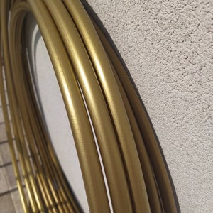 Könnte beinhalten: Ein Satz goldfarbener Metallreifen, übereinander gestapelt. Die Reifen sind glatt und glänzend, mit einer gebürsteten Oberfläche.