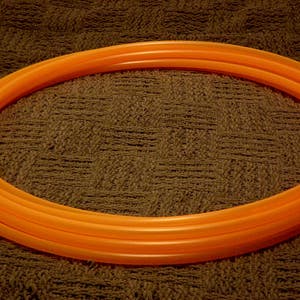 May include: A bright orange plastic hula hoop with multiple layers.
