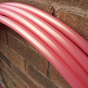 Peut inclure: Gros plan sur quatre tubes en plastique rose empilés les uns sur les autres. Les tubes sont incurvés et ont une finition brillante.