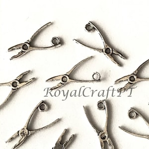 Pode incluir: Um grupo de pingentes de alicate prateados com um laço na parte superior para prender em joias ou outros artesanatos.