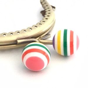 May include: Gold metal purse frame with two colorful striped round clasps. The clasps are pink, white, green, yellow, and red.