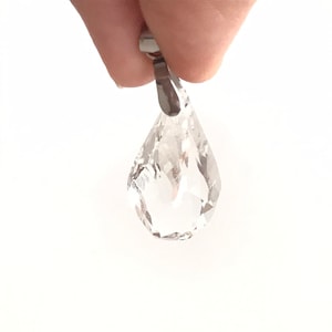 Pode incluir: Um pingente de cristal transparente em forma de lágrima com uma argola de prata.