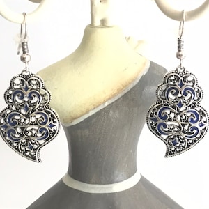 Puede incluir: Pendientes de filigrana plateada con un diseño de esmalte azul. Los pendientes tienen forma de corazón y un diseño colgante.