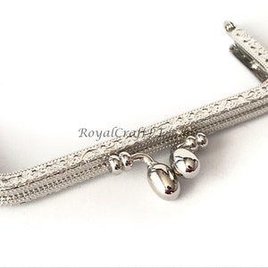 May include: Silver-toned metal purse frame with an ornate design and a dangling charm with three beads.