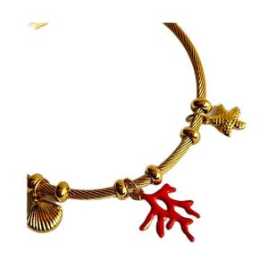 Pode incluir: Uma pulseira de ouro com três pingentes: uma concha, uma estrela do mar e um ramo de coral vermelho.
