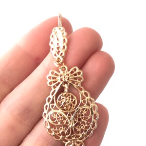 May include: Gold filigree dangle earrings with a delicate, intricate design. The earrings are made of a lightweight metal and have a classic, elegant style.