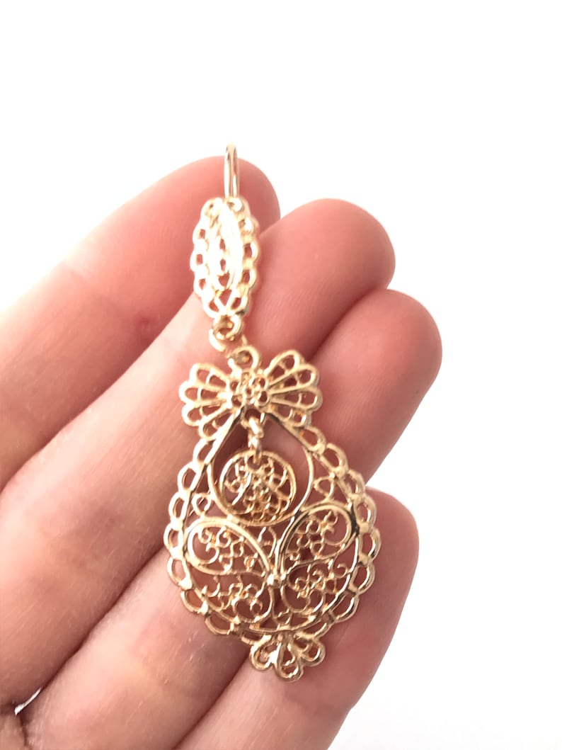May include: Gold filigree dangle earrings with a delicate, intricate design. The earrings are made of a lightweight metal and have a classic, elegant style.