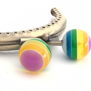 Può includere: Due chiusure per borsetta in metallo color arcobaleno con finitura argentata. Le chiusure sono rotonde e hanno un motivo a strisce di viola, giallo, verde, blu e bianco.
