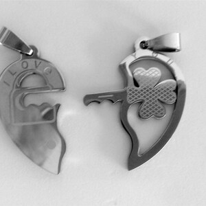 May include: Two silver heart-shaped pendants, one with a keyhole and the word "I LOVE" engraved on it, and the other with a shamrock design and a key.
