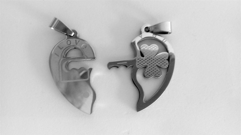 May include: Two silver heart-shaped pendants, one with a keyhole and the word "I LOVE" engraved on it, and the other with a shamrock design and a key.