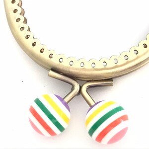 May include: A gold metal purse frame with a scalloped edge and two colorful striped buttons. The buttons are pink, red, orange, yellow, green, and purple.