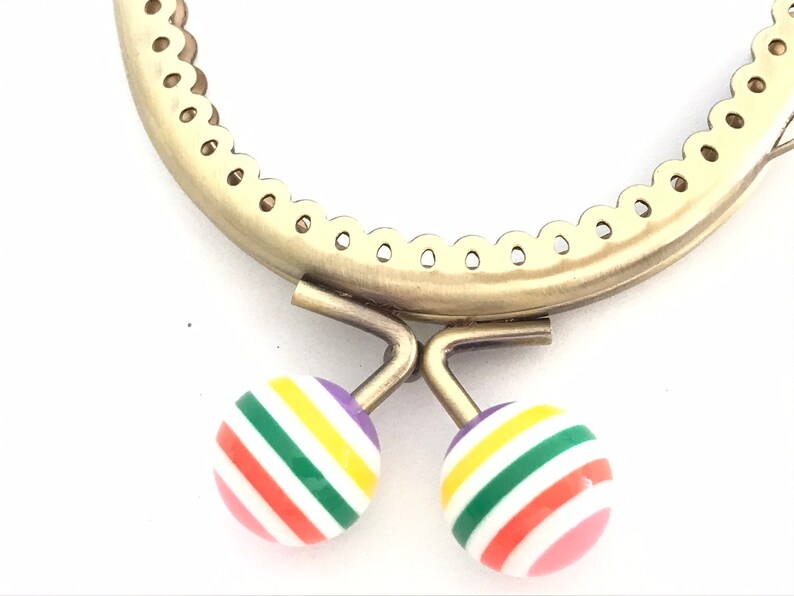 May include: A gold metal purse frame with a scalloped edge and two colorful striped buttons. The buttons are pink, red, orange, yellow, green, and purple.