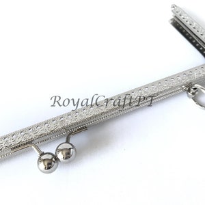 May include: Silver-toned metal purse frame with an ornate design and a ring on the side. The frame has two metal balls on the bottom.