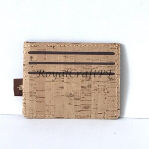 May include: A brown cork wallet with a brown stitched border and three brown elastic bands. The wallet has the text "RoyalCraftPT" printed on the front.