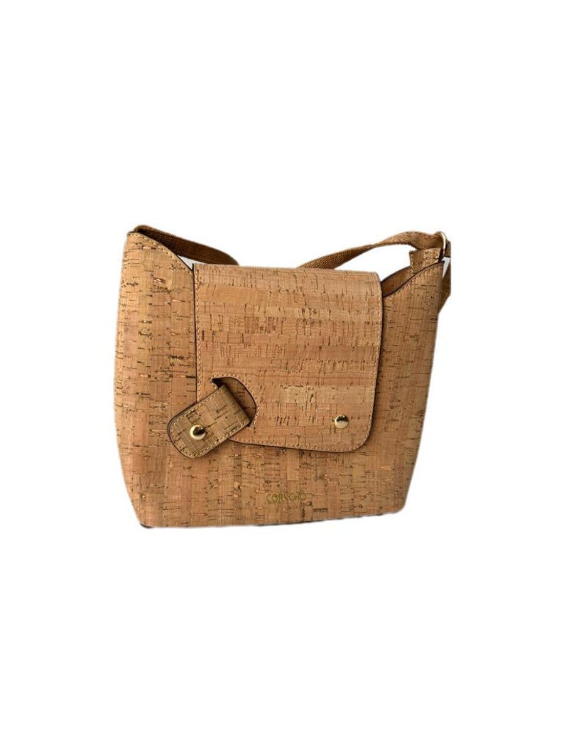 May include: A light brown cork crossbody bag with a flap closure and gold accents. The bag has a small pocket on the front and a strap that can be adjusted.