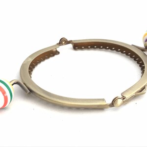 May include: A gold-toned metal purse frame with two colorful plastic round handles. The handles have a white background with red, green, yellow, and purple stripes.
