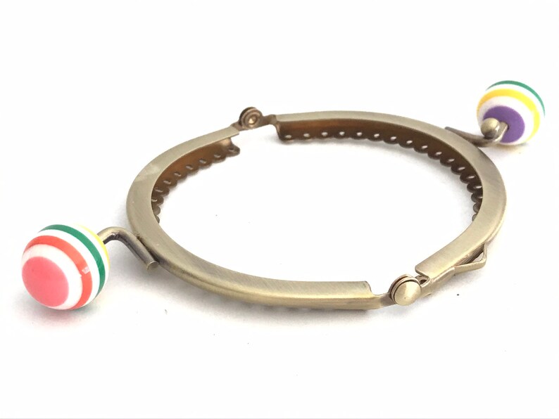 May include: A gold-toned metal purse frame with two colorful plastic round handles. The handles have a white background with red, green, yellow, and purple stripes.