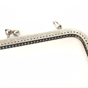 Pode incluir: Estrutura de bolsa de metal prateado com um design decorativo e dois fechos redondos de metal. A estrutura é projetada para ser usada para uma bolsa ou uma carteira de mão.