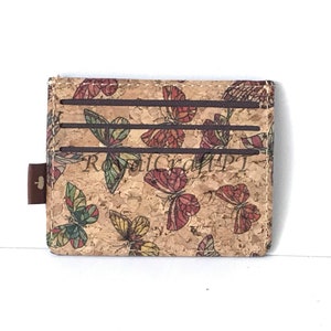 May include: A brown cork wallet with a butterfly pattern. The wallet has three card slots and a small brown leather tab.