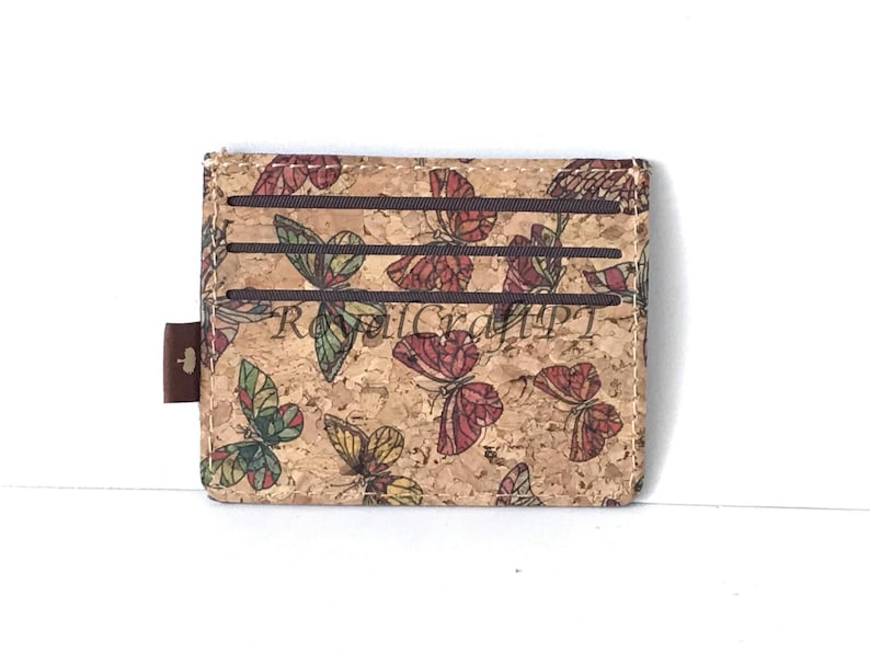 May include: A brown cork wallet with a butterfly pattern. The wallet has three card slots and a small brown leather tab.