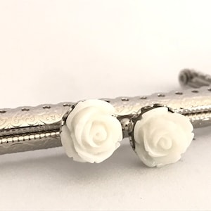 Peut inclure: Deux fermoirs de sac en forme de rose blanche sur un cadre de sac argenté.