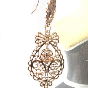 May include: Gold filigree earrings with a teardrop shape and a bow design. The earrings have a delicate, intricate design.