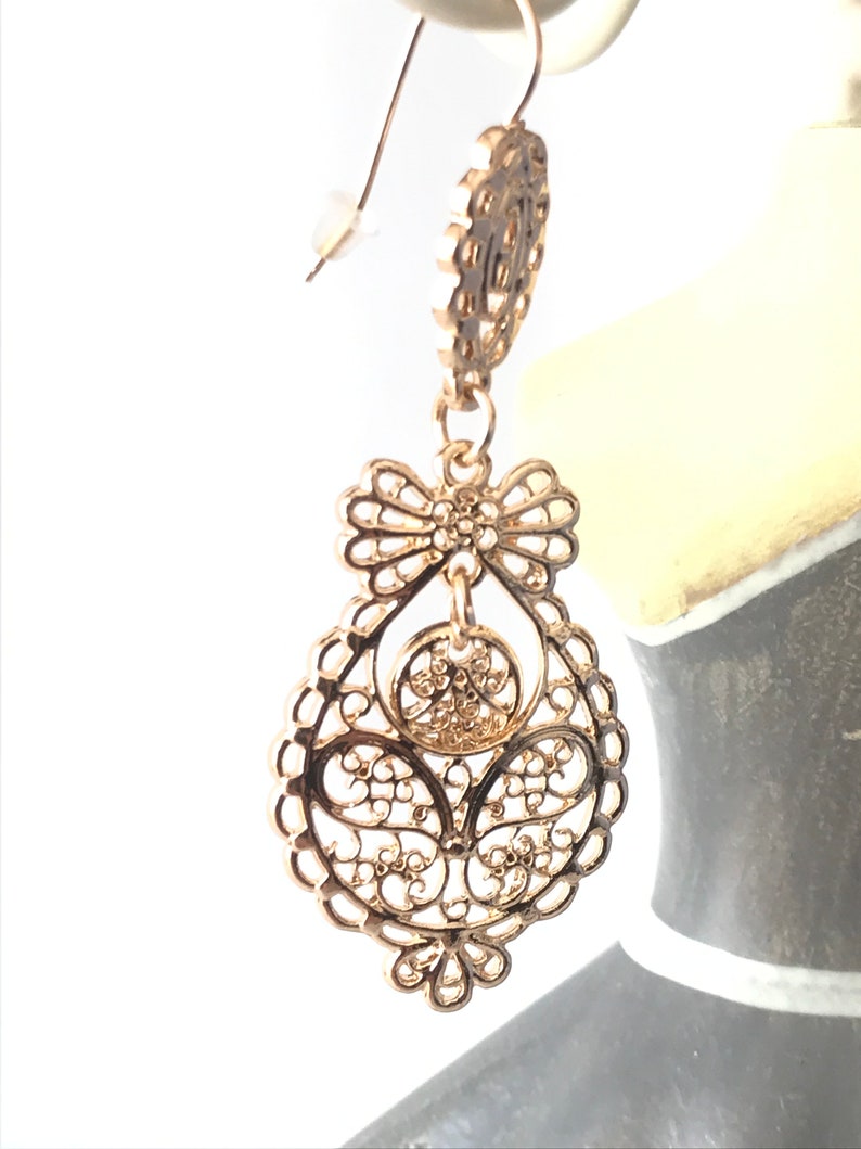 May include: Gold filigree earrings with a teardrop shape and a bow design. The earrings have a delicate, intricate design.