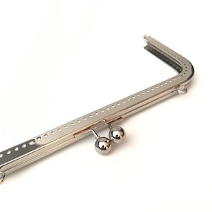 May include: Silver-toned metal purse frame with two round clasps. The frame is designed to be used for a purse or clutch.
