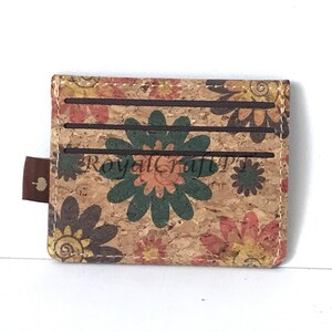 May include: A brown cork wallet with a floral pattern. The wallet has three card slots and a brown leather pull tab.