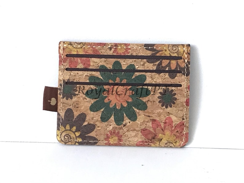 May include: A brown cork wallet with a floral pattern. The wallet has three card slots and a brown leather pull tab.