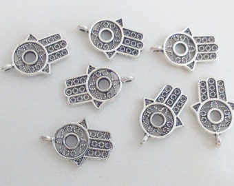 May include: Eight silver-toned metal charms in the shape of a hamsa hand, a symbol of protection and good luck. Each charm has a detailed, intricate design with a circle in the center.