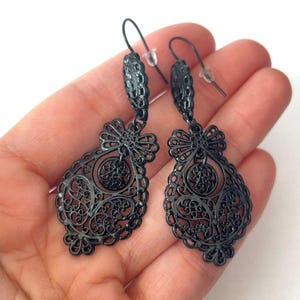 Puede incluir: Un par de pendientes de filigrana negros con forma de lágrima. Los pendientes tienen un diseño delicado e intrincado y están hechos de metal.