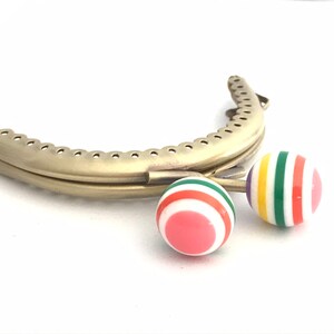 May include: Gold metal purse frame with two colorful striped plastic clasps. The clasps are red, white, green, yellow, and purple.