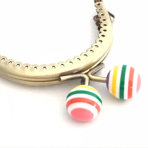 May include: Gold metal purse frame with two colorful striped plastic clasps. The clasps are red, pink, yellow, green, and white.