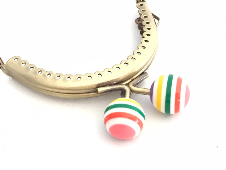 May include: Gold metal purse frame with two colorful striped plastic clasps. The clasps are red, pink, yellow, green, and white.