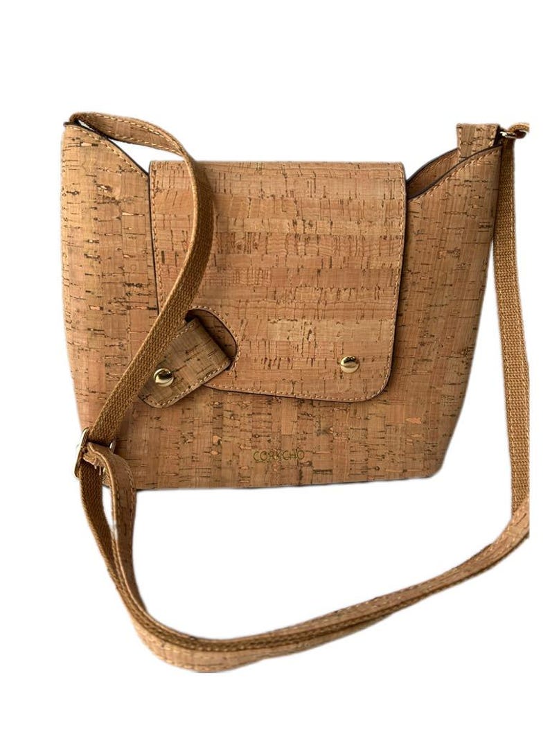 May include: A light brown cork crossbody bag with a gold logo that reads "CORKCIO".