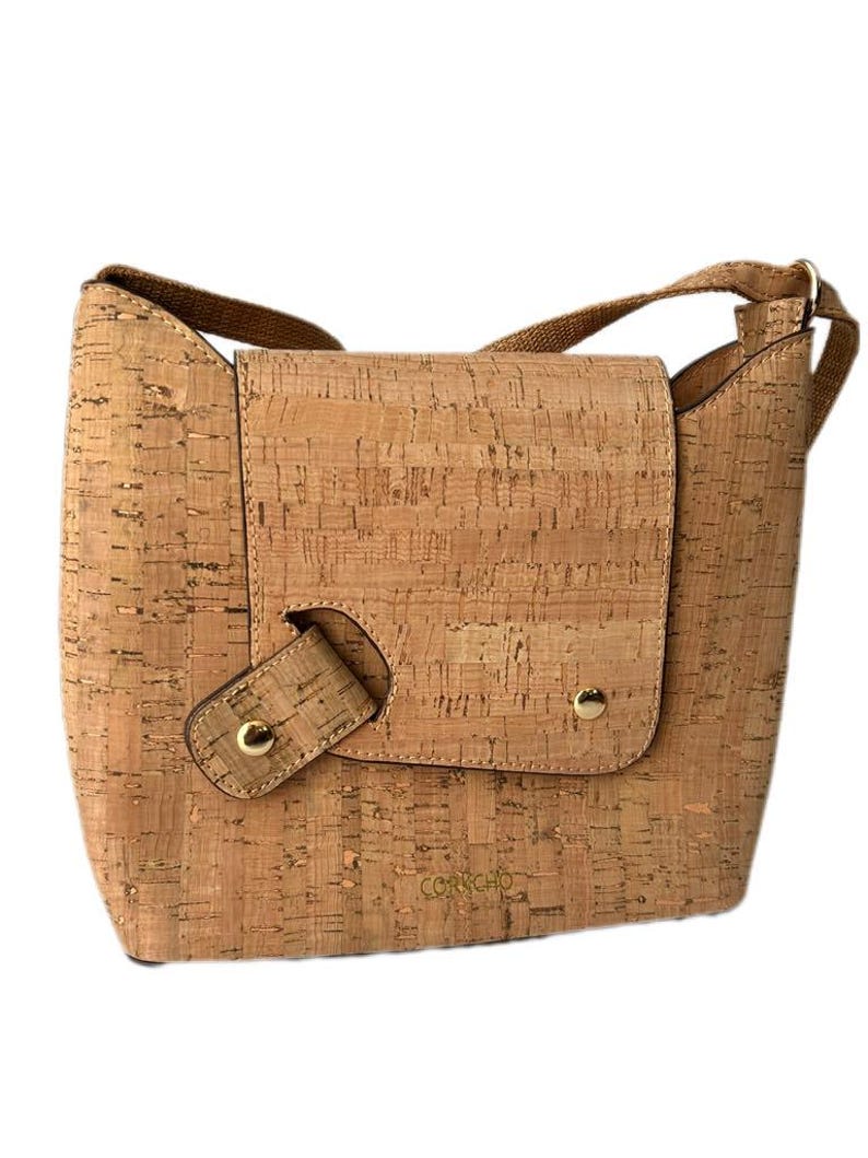 May include: A light brown cork crossbody bag with a flap closure and a gold metal buckle. The bag has a gold metal logo that says "Corkcho".