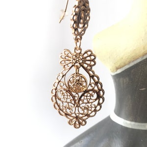 May include: Gold filigree earrings with a bow design. The earrings are dangling and have a delicate, intricate pattern.