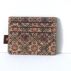 May include: A brown cork card holder with a patterned design featuring red, blue, and white geometric shapes. The card holder has a brown leather tab.