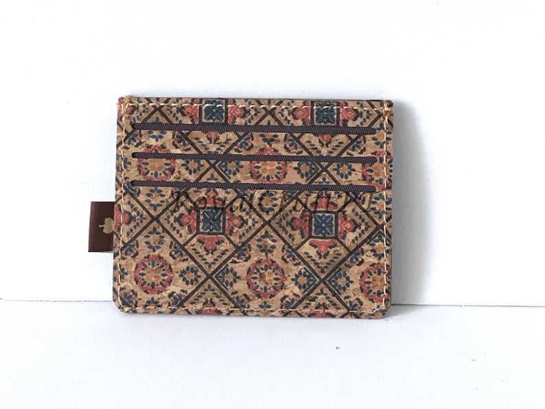 May include: A brown cork card holder with a patterned design featuring red, blue, and white geometric shapes. The card holder has a brown leather tab.