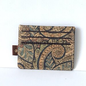 May include: A brown, cork wallet with a paisley pattern in shades of brown, blue, and green. The wallet has multiple card slots and a brown leather pull tab.