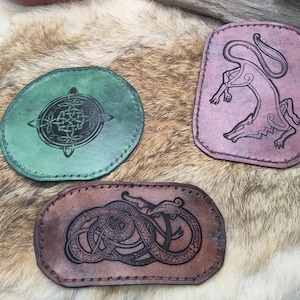 May include: Three leather patches with different designs. The first patch is green with a Celtic knot design. The second patch is brown with a snake design. The third patch is pink with a wolf design.