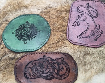 May include: Three leather patches with different designs. The first patch is green with a Celtic knot design. The second patch is brown with a snake design. The third patch is pink with a wolf design.