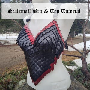 May include: A black and red scalemail bra and top displayed on a white mannequin. The top is made of overlapping scales, with black scales in the center and red scales outlining the edges. The text "Scalemail Bra & Top Tutorial" is displayed above the top.