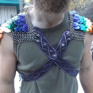 May include: Shoulder armour featuring rainbow-coloured scales and silver chainmail. The harness is black leather with purple geometric detailing. The person is wearing a green vest top.