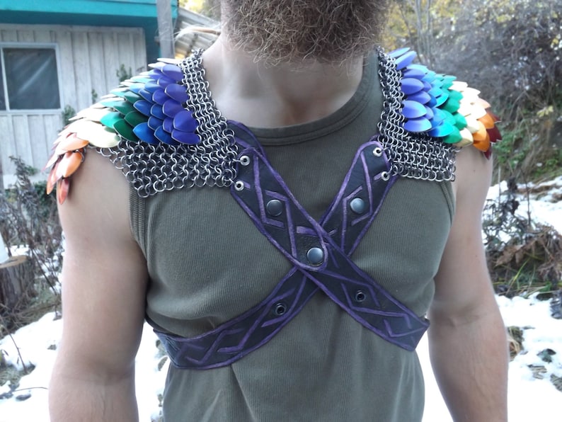 May include: Shoulder armour featuring rainbow-coloured scales and silver chainmail. The harness is black leather with purple geometric detailing. The person is wearing a green vest top.