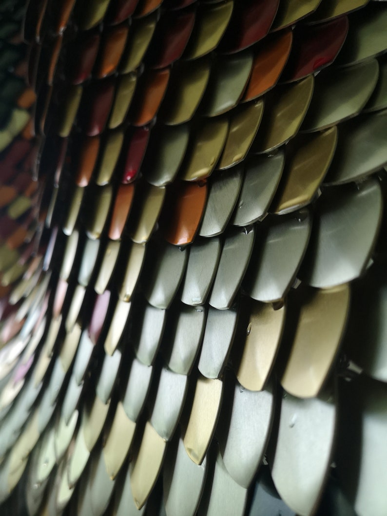 May include: Close-up of a metallic chainmail with scales in shades of gold, silver, and red.