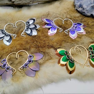 May include: Four pairs of ear cuffs with different coloured metal scales. The ear cuffs are made of metal and have a curved shape. The scales are arranged in a fan shape and are attached to the ear cuff with small rings. The ear cuffs are a popular accessory for people who want to add a touch of style to their look.