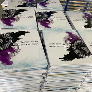 K&ouml;nnte beinhalten: Ein Stapel wei&szlig;er B&uuml;cher mit einem blauen und wei&szlig;en Aquarelldesign auf dem Cover. Der Titel des Buches lautet "The Illustrated Book of Runes".