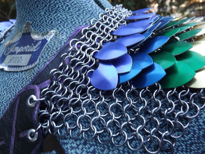 May include: A close-up of a piece of armour with a chainmail collar and layered metal scales in blue, green, and gold. The armour is attached to a black leather base with purple trim. The word "Imperial" is visible on a tag.